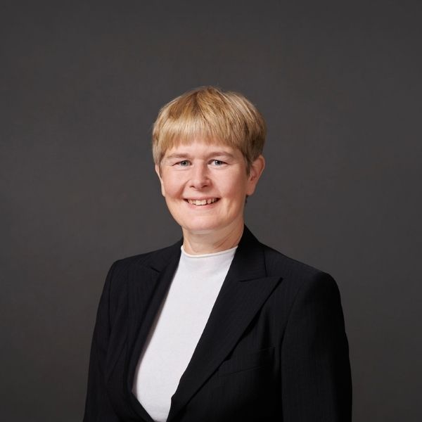 Frau mit kurzen blonden Haaren l&auml;chelt vor grauem Hintergrund