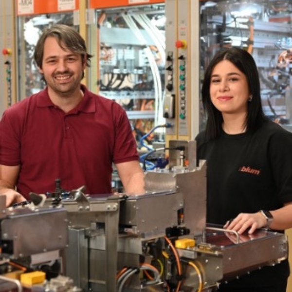 Mann und Frau in Arbeitskleidung stehen nebeneinander vor einer Industriemaschine